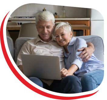 a happy older couple sitting together on a couch in their living room smiling at an open laptop